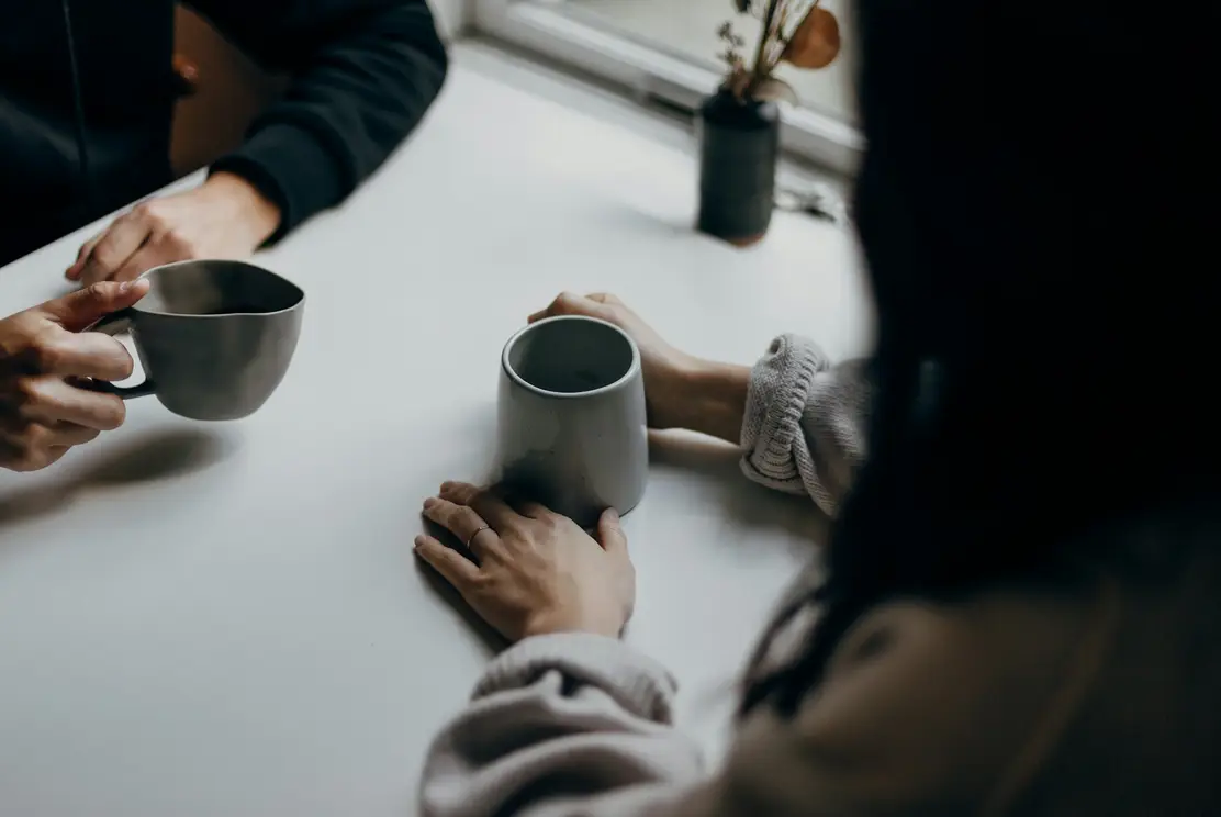 Two people sitting at a table with mugs of tea