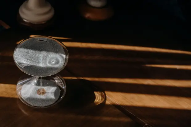 A sand timer on a wooden table in morning sunlight