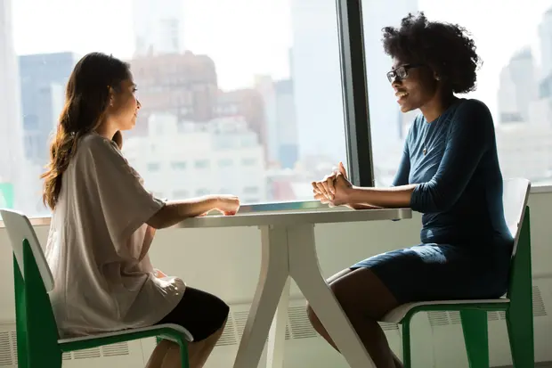 Two women in conversation at a table overlooking a city