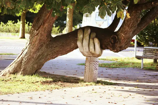 A carved wooden hand supporting the trunk of a leaning tree